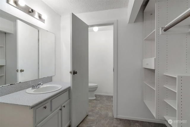 bathroom with a textured ceiling, vanity, and toilet