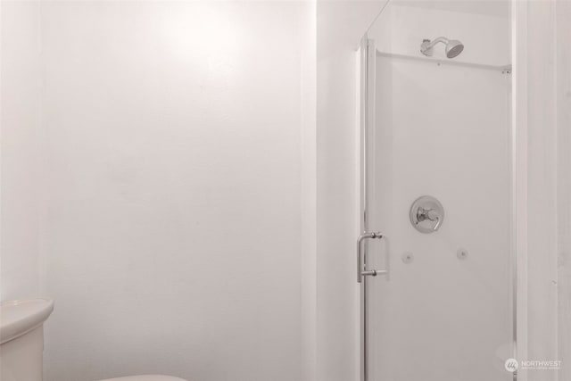 bathroom featuring a shower with door and toilet