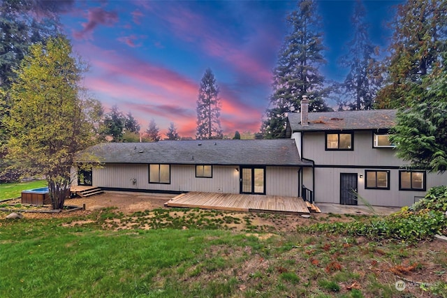 back house at dusk featuring a lawn and a wooden deck