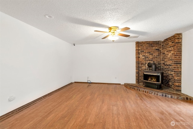 unfurnished living room with a wood stove, ceiling fan, hardwood / wood-style flooring, and a textured ceiling