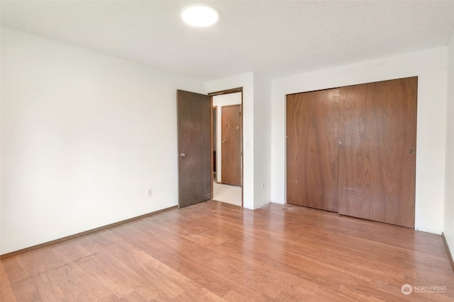 unfurnished bedroom featuring a textured ceiling, a closet, and light hardwood / wood-style flooring