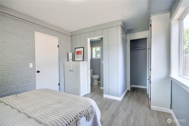 bedroom featuring ensuite bathroom, light hardwood / wood-style flooring, a closet, and brick wall