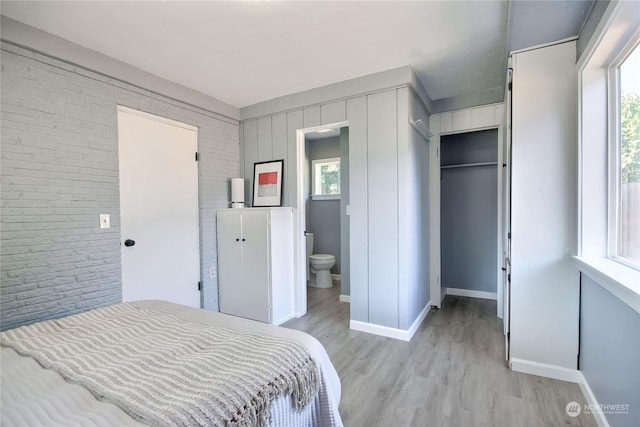 bedroom with light wood finished floors, baseboards, brick wall, and connected bathroom