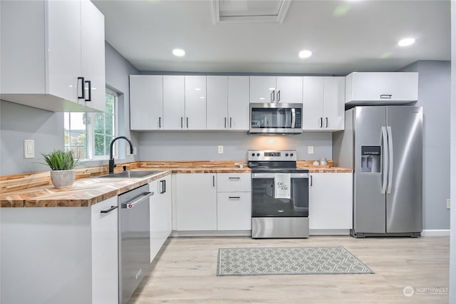 kitchen featuring butcher block countertops, a sink, stainless steel appliances, light wood-style flooring, and white cabinetry