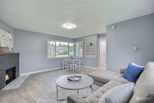 living room with wood finished floors, a textured ceiling, baseboards, and a lit fireplace