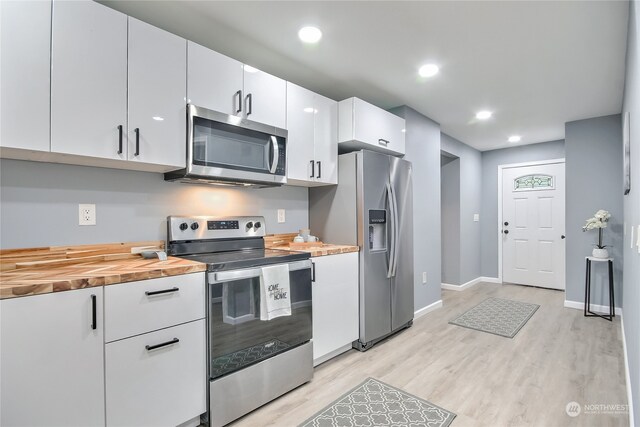 kitchen featuring light wood-type flooring, white cabinetry, stainless steel appliances, and wooden counters