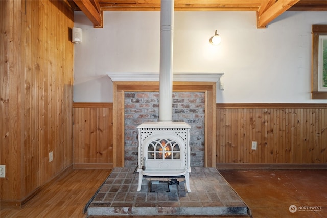 room details featuring wooden walls, beam ceiling, wood-type flooring, and a wood stove