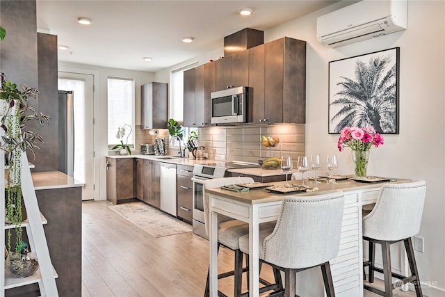 kitchen with dark brown cabinets, stainless steel appliances, a wall unit AC, and light wood-type flooring