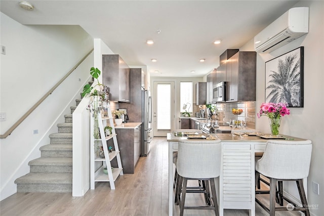 kitchen featuring appliances with stainless steel finishes, a kitchen breakfast bar, tasteful backsplash, kitchen peninsula, and an AC wall unit