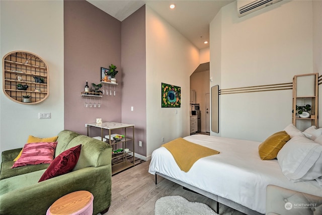 bedroom with an AC wall unit, a high ceiling, and light hardwood / wood-style floors