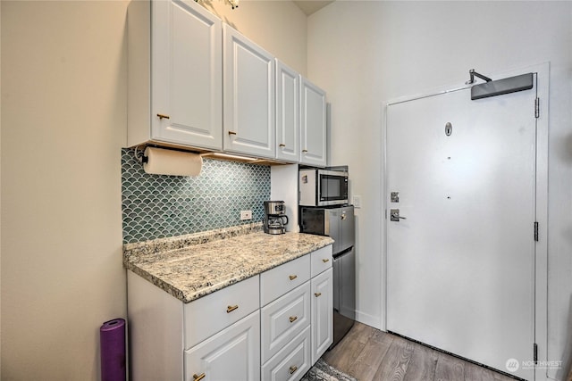 kitchen with light hardwood / wood-style floors, light stone countertops, tasteful backsplash, and white cabinets