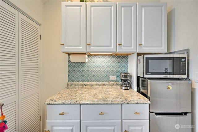 kitchen with light stone countertops, white cabinetry, appliances with stainless steel finishes, and tasteful backsplash