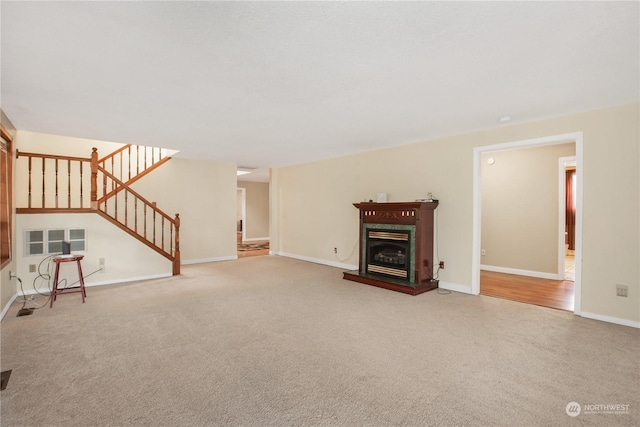 unfurnished living room with baseboards, stairway, a fireplace with raised hearth, and carpet