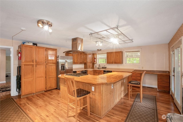 kitchen featuring island exhaust hood, a kitchen island, a kitchen bar, appliances with stainless steel finishes, and a sink