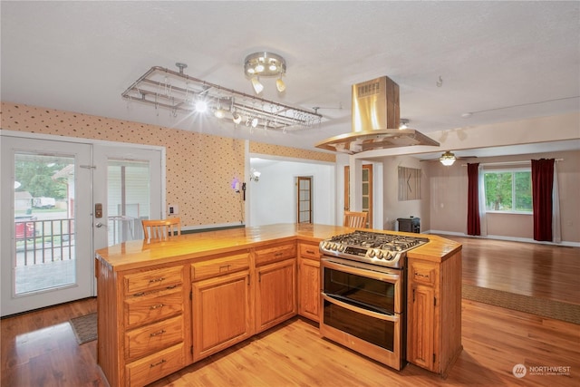 kitchen featuring butcher block countertops, double oven range, island exhaust hood, open floor plan, and light wood finished floors