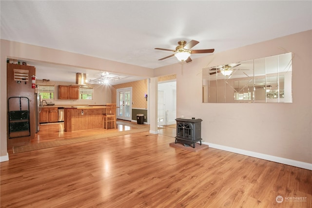 unfurnished living room with a wood stove, light wood-style flooring, baseboards, and a ceiling fan
