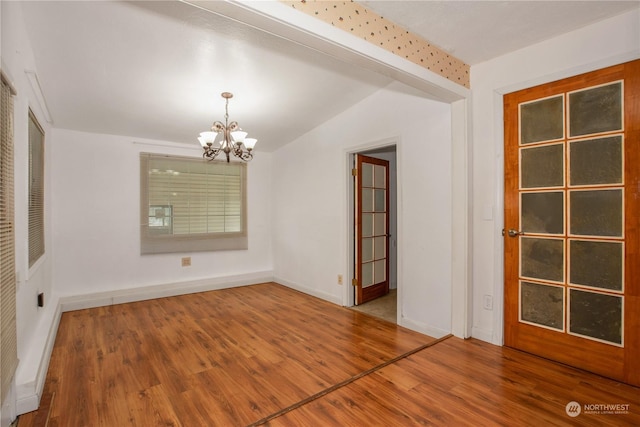 empty room featuring baseboards, wood finished floors, a notable chandelier, and vaulted ceiling