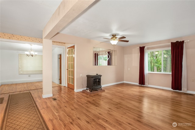 unfurnished living room with wood-type flooring, ceiling fan with notable chandelier, and a wood stove