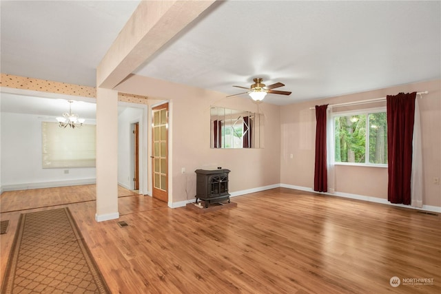 unfurnished living room featuring visible vents, a wood stove, wood finished floors, and ceiling fan with notable chandelier