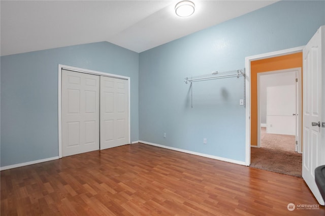 unfurnished bedroom featuring wood finished floors, baseboards, a closet, and lofted ceiling