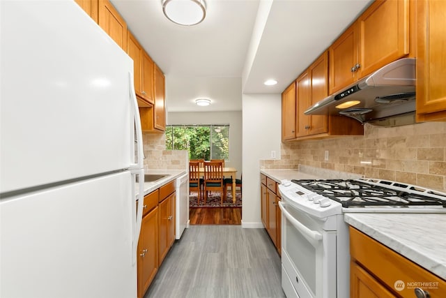 kitchen featuring light stone counters, light wood-type flooring, backsplash, and white appliances