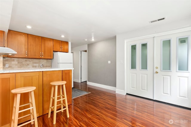 kitchen featuring white refrigerator, a breakfast bar area, tasteful backsplash, and dark hardwood / wood-style flooring