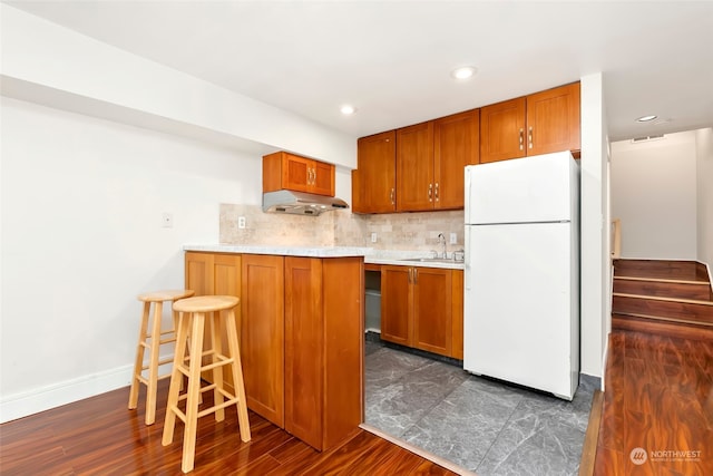 kitchen with dark wood-type flooring, tasteful backsplash, white fridge, a kitchen bar, and sink