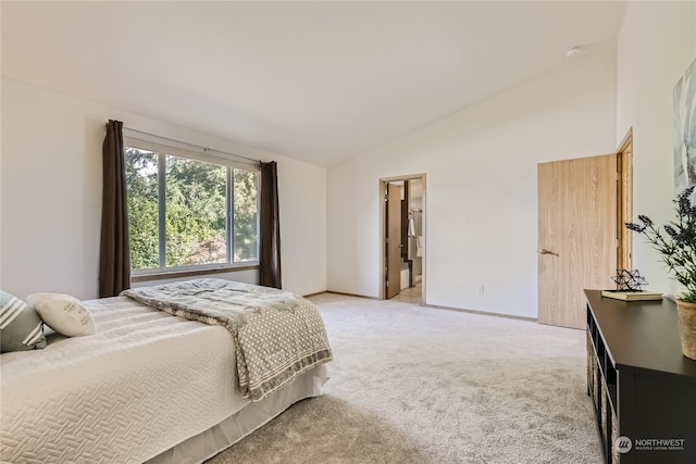 carpeted bedroom featuring vaulted ceiling and ensuite bath