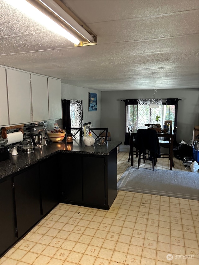 kitchen featuring a textured ceiling, hanging light fixtures, and white cabinets