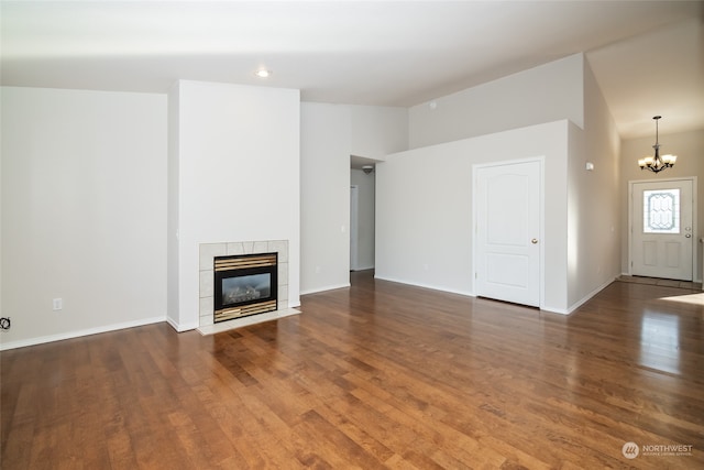 unfurnished living room with a tiled fireplace, dark hardwood / wood-style floors, a towering ceiling, and a notable chandelier