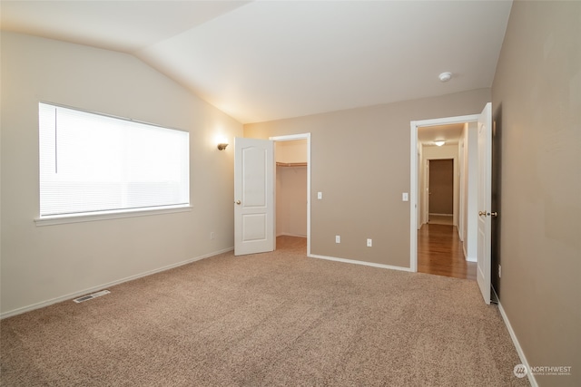 unfurnished bedroom with carpet floors, vaulted ceiling, a walk in closet, and a closet