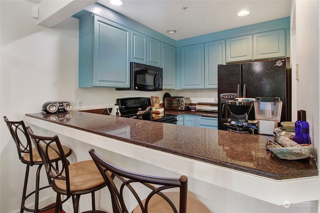 kitchen featuring kitchen peninsula, black appliances, blue cabinetry, dark stone counters, and a kitchen bar