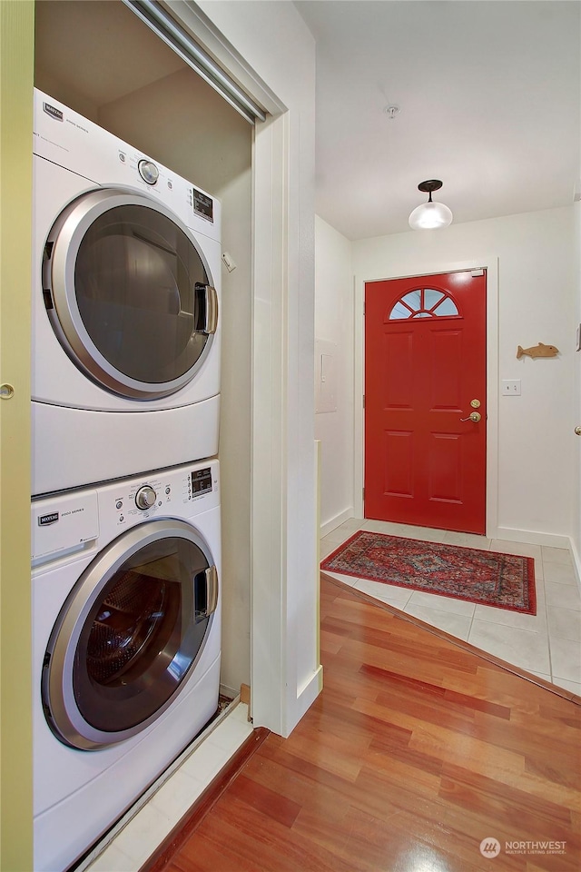 laundry room featuring stacked washer and dryer, laundry area, baseboards, and light wood-style floors
