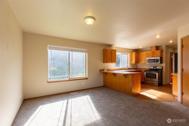 kitchen with sink, kitchen peninsula, appliances with stainless steel finishes, a breakfast bar, and light carpet