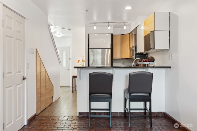 kitchen with a kitchen bar, white cabinets, and stainless steel refrigerator