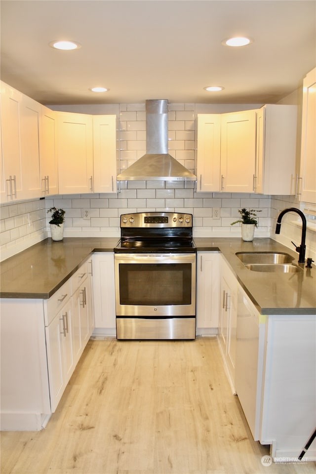 kitchen with wall chimney exhaust hood, sink, light hardwood / wood-style floors, white cabinetry, and stainless steel electric range