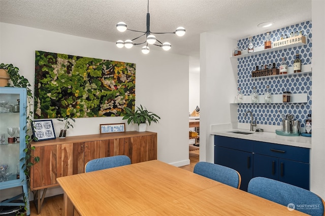 dining space featuring a notable chandelier, a textured ceiling, sink, and hardwood / wood-style flooring