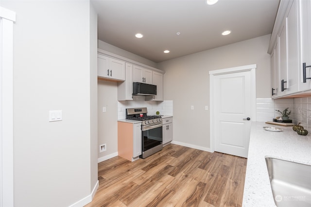 kitchen featuring gas stove, decorative backsplash, white cabinetry, and light hardwood / wood-style flooring