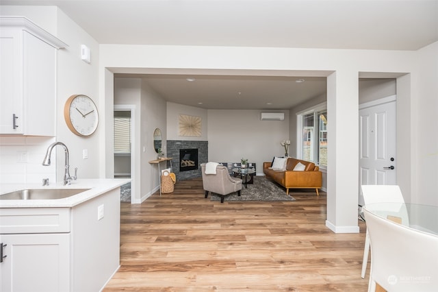 living room featuring a stone fireplace, light wood-type flooring, sink, and an AC wall unit