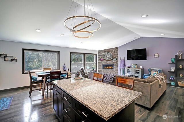 kitchen with lofted ceiling, a kitchen island, a stone fireplace, dark hardwood / wood-style floors, and light stone countertops