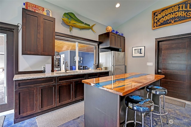 kitchen with vaulted ceiling, stainless steel refrigerator, a kitchen island, dark brown cabinets, and sink