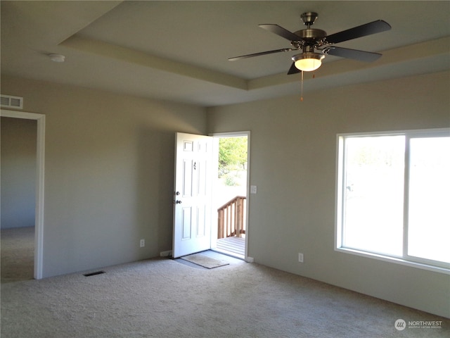 carpeted spare room featuring ceiling fan, a tray ceiling, and plenty of natural light