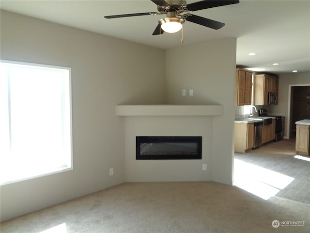 unfurnished living room with ceiling fan, light colored carpet, and sink