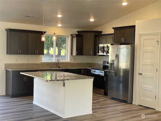 kitchen featuring a kitchen island, vaulted ceiling, appliances with stainless steel finishes, dark stone counters, and light wood finished floors