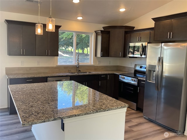 kitchen with light wood finished floors, appliances with stainless steel finishes, dark stone countertops, dark brown cabinets, and a sink