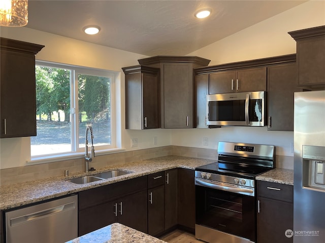 kitchen featuring appliances with stainless steel finishes, vaulted ceiling, light stone countertops, dark brown cabinetry, and sink