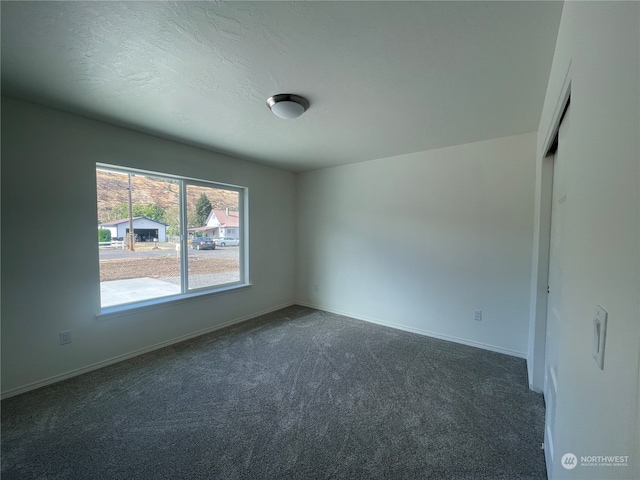 spare room with dark carpet, a textured ceiling, and baseboards