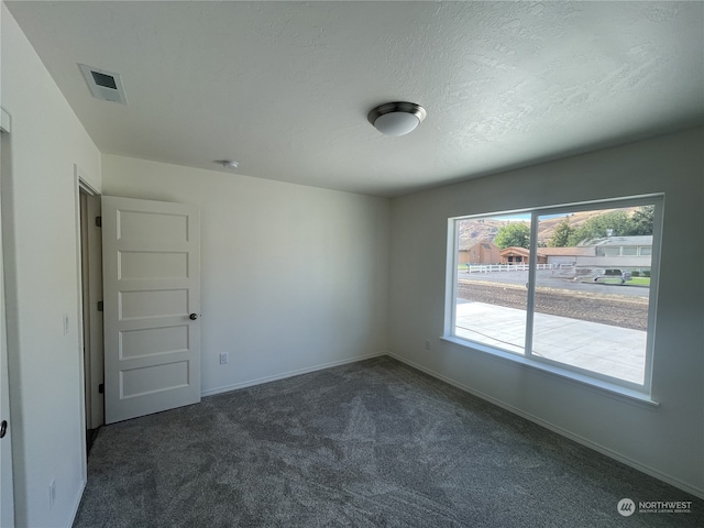 spare room with baseboards, visible vents, dark colored carpet, and a textured ceiling