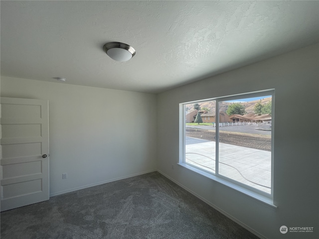 unfurnished room with baseboards, dark carpet, and a textured ceiling