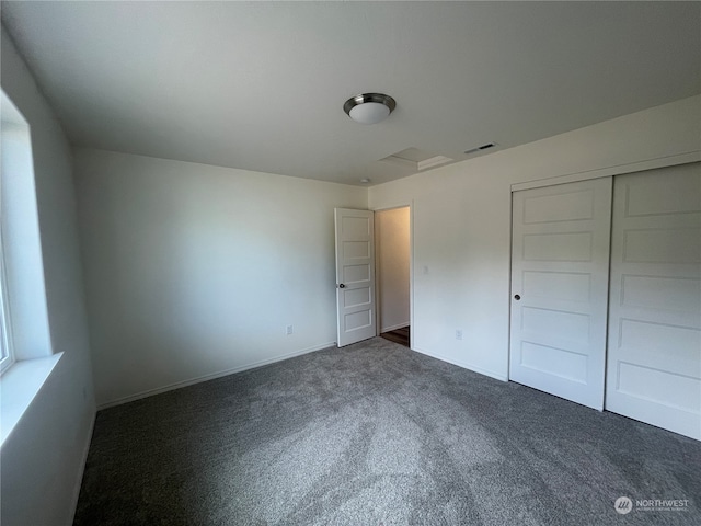 unfurnished bedroom featuring baseboards, visible vents, dark colored carpet, and a closet